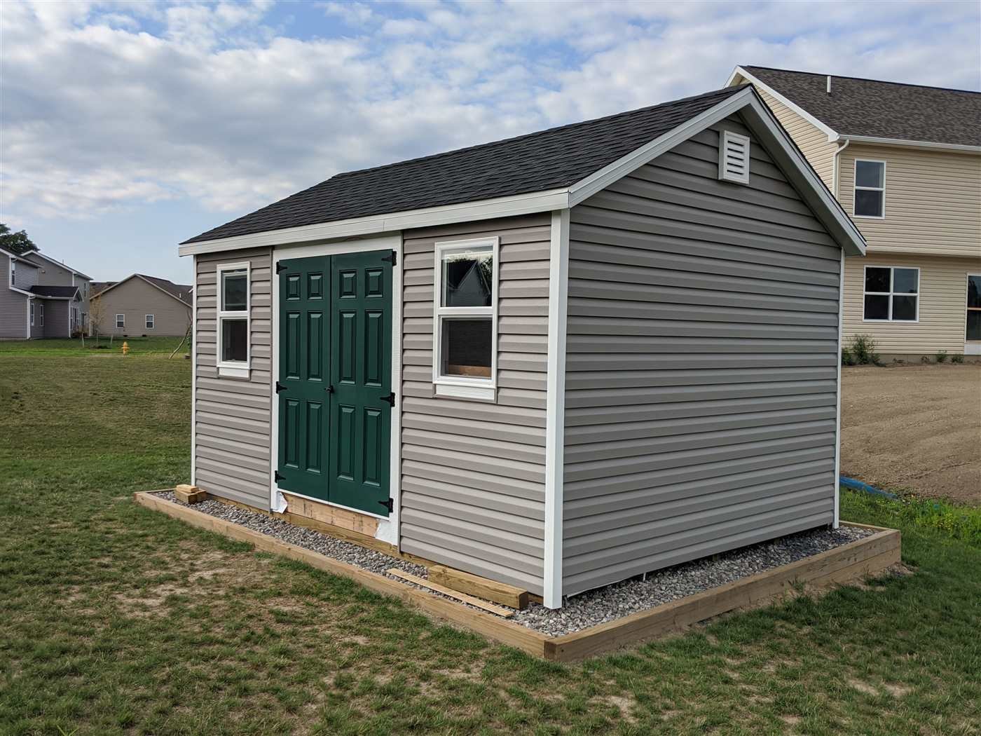 The finished shed: gray siding, green double doors, and white trim on a gravel pad.